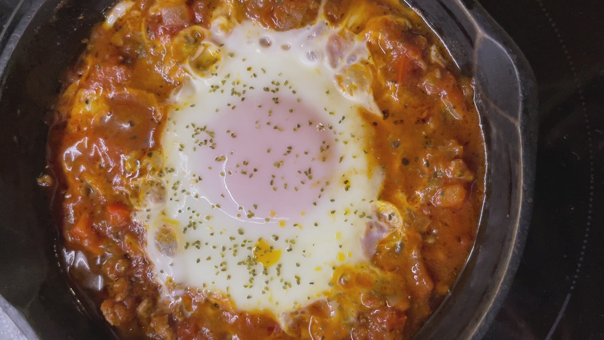 An egg in tomato sauce bubbling in a cast iron pot sprinkled with Seagreens Ruby One