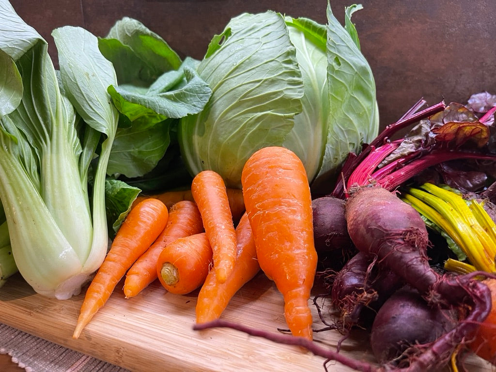 Assorted home grown vegetables including carrots, beetroot, and cabbage on a wooden surface.
